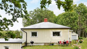 Une maison de plain-pied avec un toit en pente, un petit porche et un mur de pierre en premier plan.