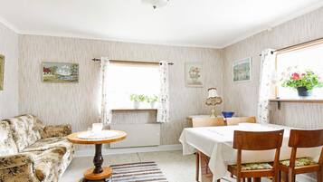 A cozy living room with a floral sofa, a round wooden table, and a dining table with chairs.