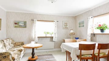 Uma sala de estar aconchegante com sofá, mesa de madeira redonda, mesa de jantar com cadeiras e uma janela com cortinas.