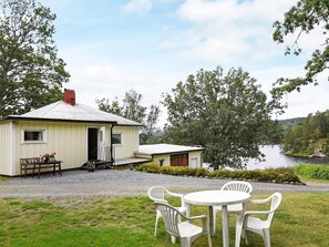 A small house with a gravel driveway, a patio with chairs, and a view of a lake. - 5 Person Holiday Home in Bullaren (Bullaren)