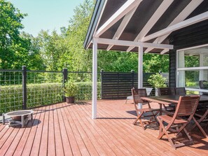 Een houten terras met een tafel, stoelen, een overdekt gedeelte en uitzicht op groen.