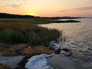 Un paisaje natural con una masa de agua, zonas verdes y un atardecer.