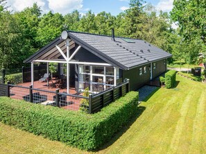Et moderne hus med en overdækket terrasse, en indhegnet have og en velholdt græsplæne.