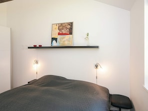 A bedroom with a bed, a shelf with artwork, and wall-mounted lights. - 5 Star Holiday Home in Hadsund (Hadsund)