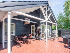 A covered outdoor deck with a table and chairs, a grill, and a ladder leading to a covered porch. - 5 Star Holiday Home in Hadsund (Hadsund)