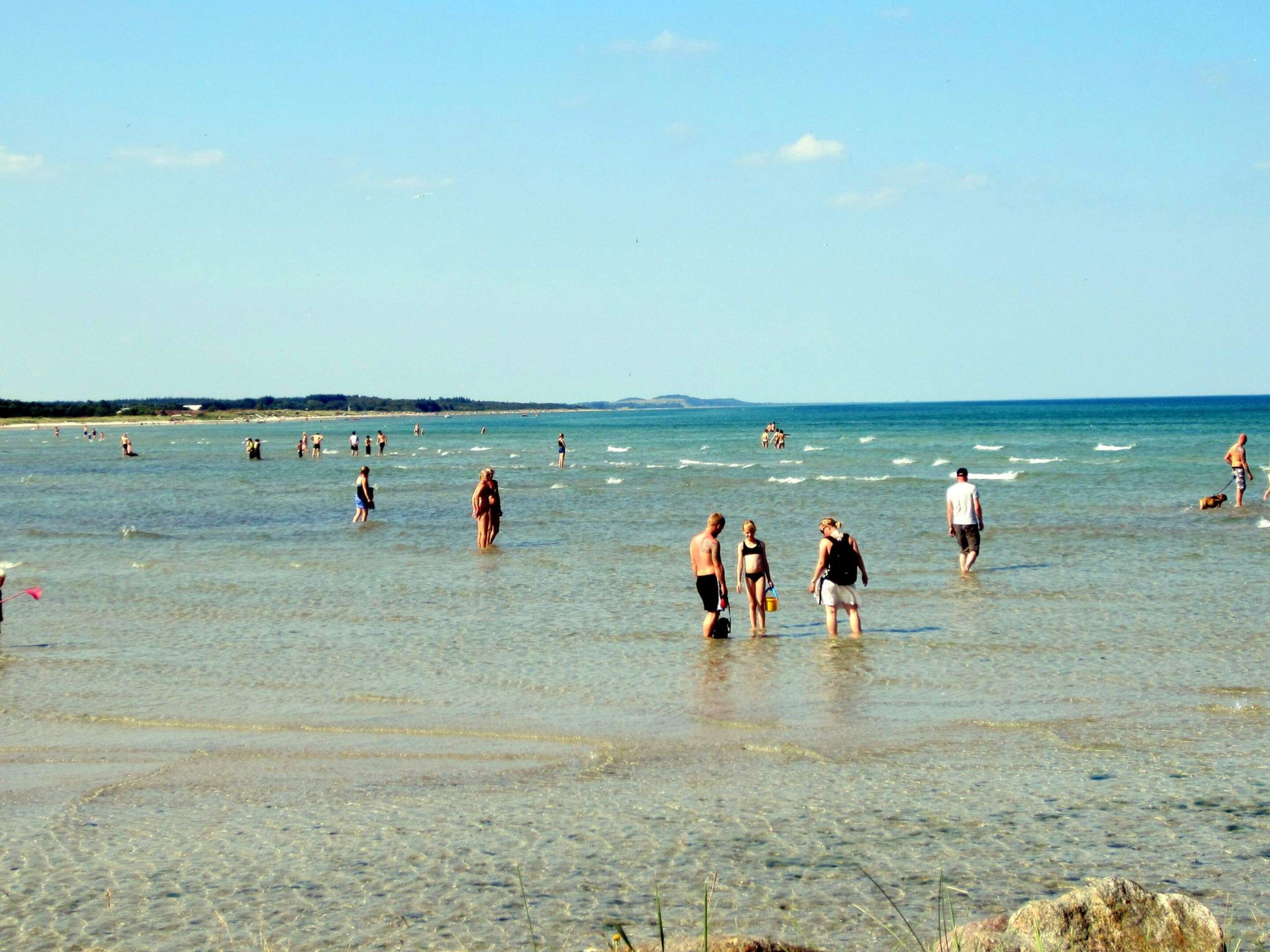 A beach with people in the water and on the shore, clear skies, and distant land.