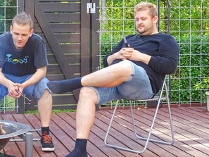 Two individuals seated on a deck with a fire pit and metal chairs. - 5 Star Holiday Home in Hadsund (Hadsund)