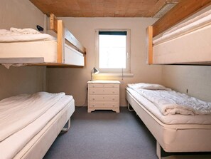 Quarto pequeno e compacto com beliches, uma cômoda e uma janela que traz luz natural.