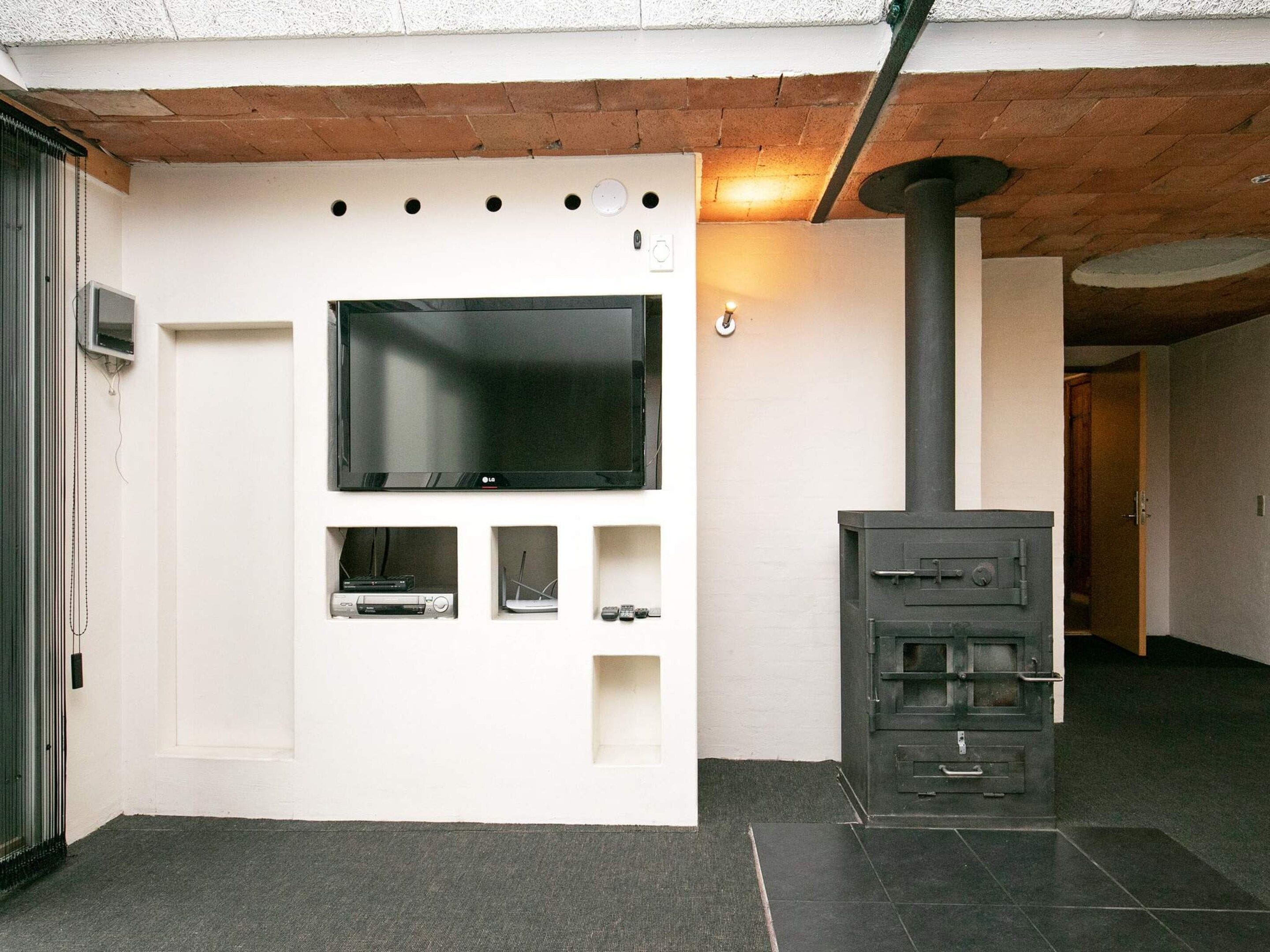 Un espacio moderno para vivir con un televisor de pantalla plana montado en una pared blanca, una chimenea empotrada y un mueble de entretenimiento pequeño debajo del televisor.