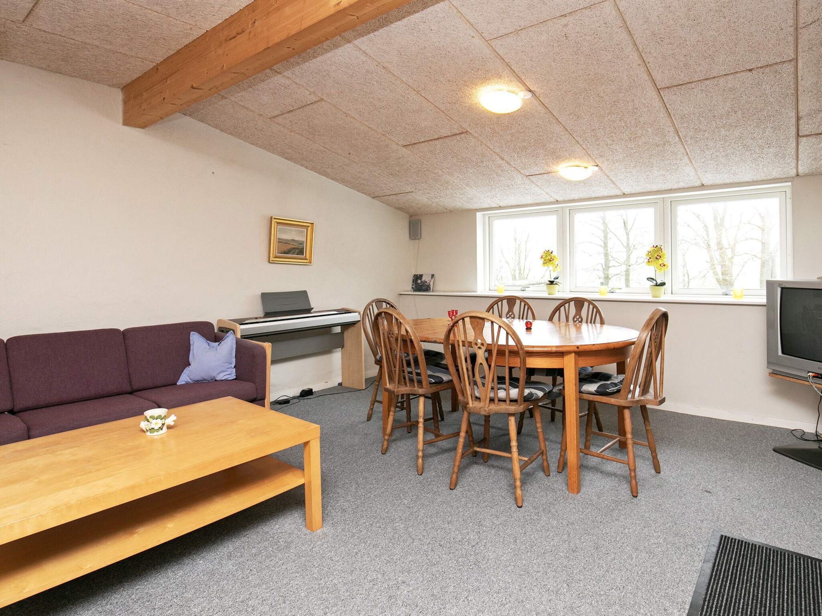 Ein Zimmer mit einem Holztisch und Stühlen, einer Couch, einem Schreibtisch mit Computer und einem Fernseher.