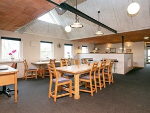 A spacious dining area with wooden tables and chairs, a kitchen area with a bar, and large windows allowing natural light.