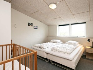A room with a crib, two beds, a window, and a nightstand.