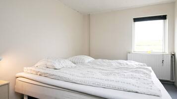 Habitación individual con una cama blanca, una mesita de noche y una ventana con vistas al exterior.