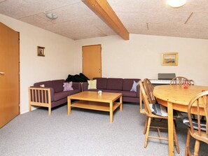 A room with a wooden ceiling, a sofa, a coffee table, a dining table with chairs, a keyboard, and a framed picture on the wall.