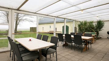 Un espacio de comedor al aire libre con mesas y sillas, vista al campo y un edificio al fondo.