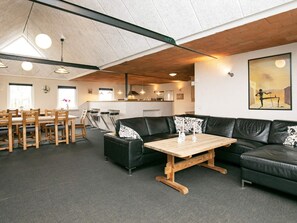 A modern living room with a black leather sofa, wooden coffee table, and a dining area with wooden chairs and a table. - 4 Star Holiday Home in Logstor (Logstor)