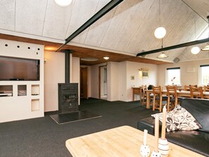 Uma sala de estar com lareira, televisão de tela plana, área de jantar com móveis de madeira e sofá de couro preto.