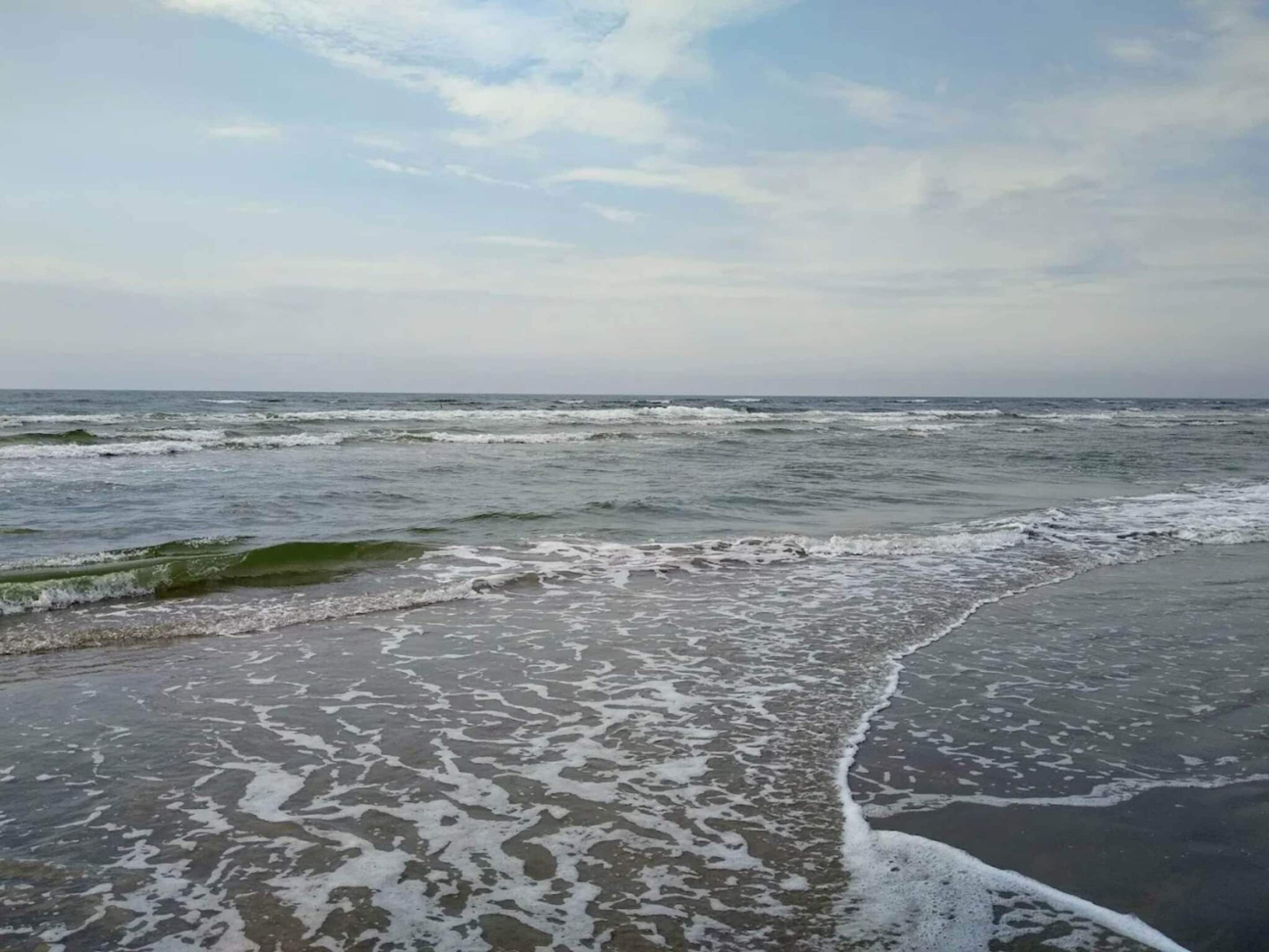 A beach with waves approaching the shore, a clear sky, and no visible structures or people.