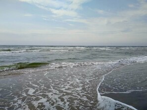 Een strand met golven die de kust naderen, een heldere lucht en geen zichtbare gebouwen of personen.