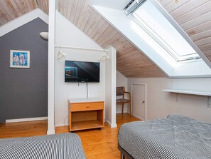 A room with a sloped ceiling, a television mounted on the wall, a wooden cabinet, a chair, and a bed with striped bedding.