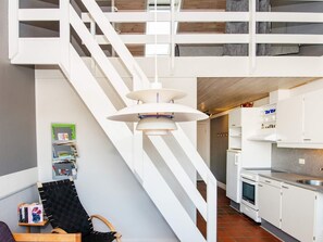 A modern interior with a staircase, a kitchen area, and a reading nook with books and a chair.