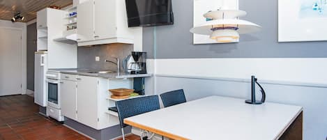 A compact kitchen with white cabinets, a built-in oven, a coffee maker, and a flat-screen TV mounted on the wall.
