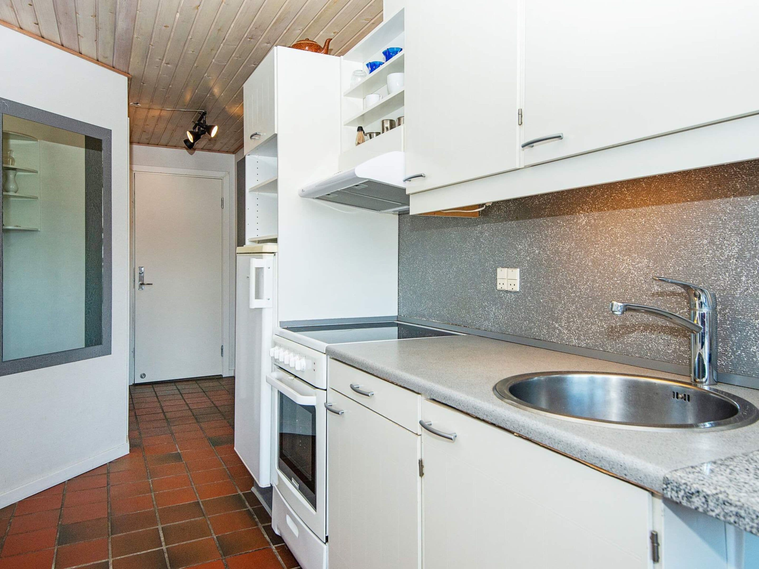 Cozinha compacta com armários brancos, pia de aço inoxidável e painel de azulejos.