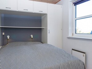 Een slaapkamer met een bed, inbouwledingkast, nachtlampjes en een raam.