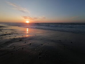A beach with the sun setting over the horizon, waves gently lapping at the shore.