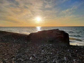 A pebbled beach with a large rock in the foreground and the sun setting over the water. - 5 Star Holiday Home in Frostrup (Frøstrup)