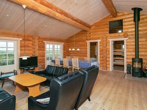 A log cabin interior with a dining area, seating, a TV, and a wood stove.