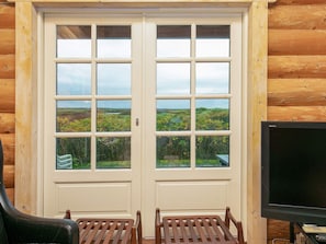 A wooden cabin with a large windowed door, two wooden chairs, and a television. - 5 Star Holiday Home in Frostrup (Frøstrup)