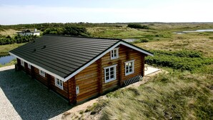 A log cabin with a sloped roof, a gravel driveway, and a pond in the background. - 5 Star Holiday Home in Frostrup (Frøstrup)