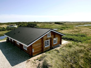 A log cabin with a sloped roof, a gravel driveway, and a pond in the background. - 5 Star Holiday Home in Frostrup (Frøstrup)
