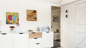 A white kitchen with a wooden cabinet, a radio, and a painting on the wall.