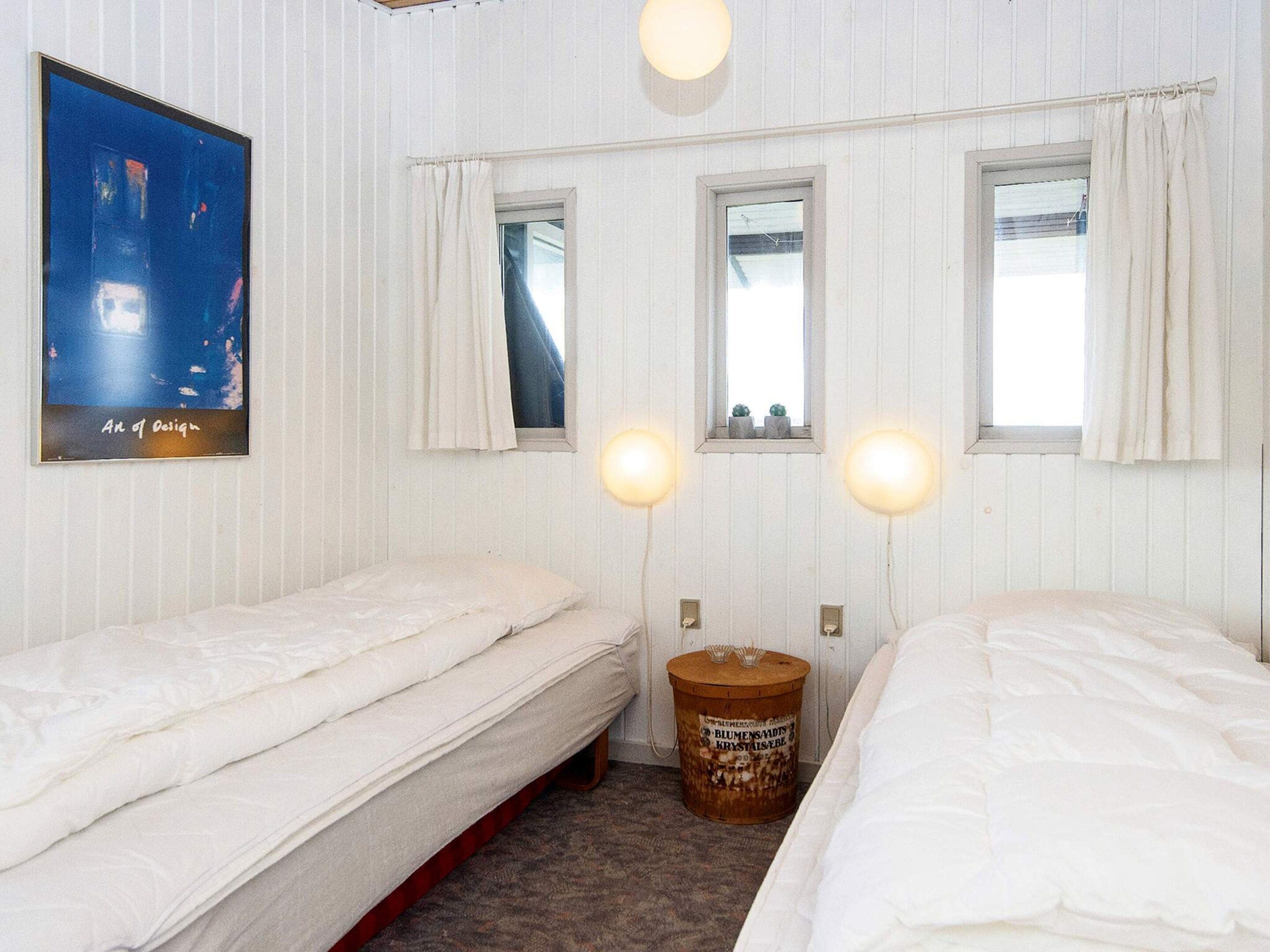 A hotel room with two single beds, a poster on the wall, and two windows with curtains.