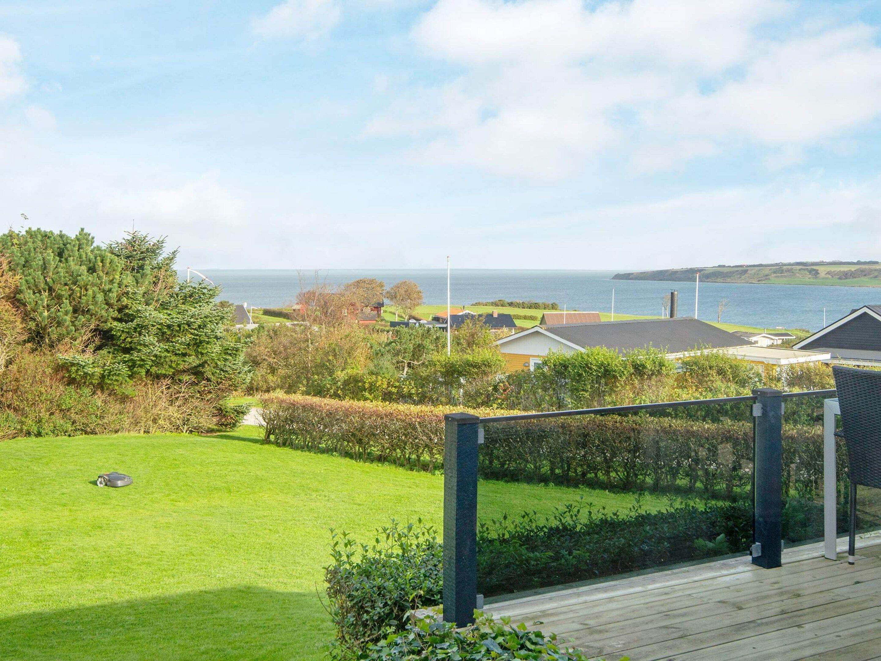 Una propiedad residencial con vista al mar, una terraza de madera y un césped bien cuidado.