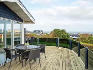 Eine Terrasse mit Tisch und Stühlen, die auf einen Wohnbereich mit Häusern und Blick aufs Meer blickt.