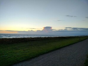 A coastal road with a grassy verge and a gravel path leading to the sea.