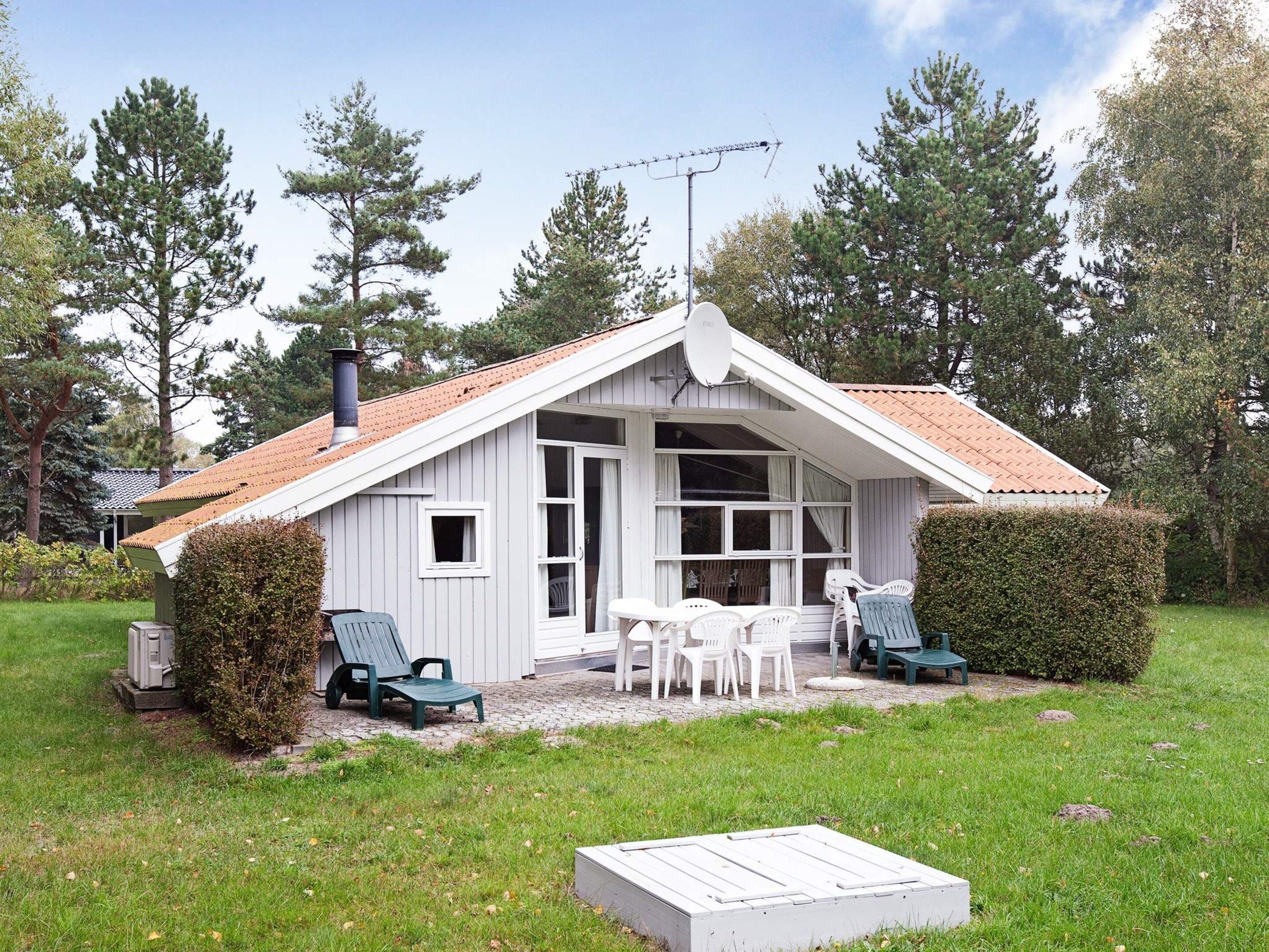A small, single-story building with a sloped roof, a chimney, and a patio area with outdoor furniture.