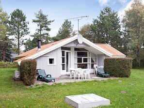 A small, single-story building with a sloped roof, a chimney, and a patio area with outdoor furniture. - Quiet Holiday Home in Rodby near Sea (Rodby)