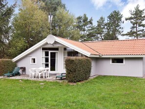 A single-story building with a sloped roof, a small porch with chairs, and a hedge in front. - Quiet Holiday Home in Rodby near Sea (Rodby)