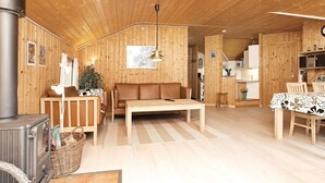 A cozy cabin interior with a wood stove, sofa, dining table, and kitchen area.