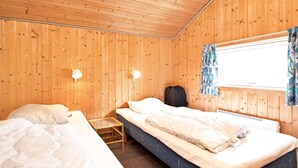 A wooden cabin room with two beds, a small table, and a window with curtains.