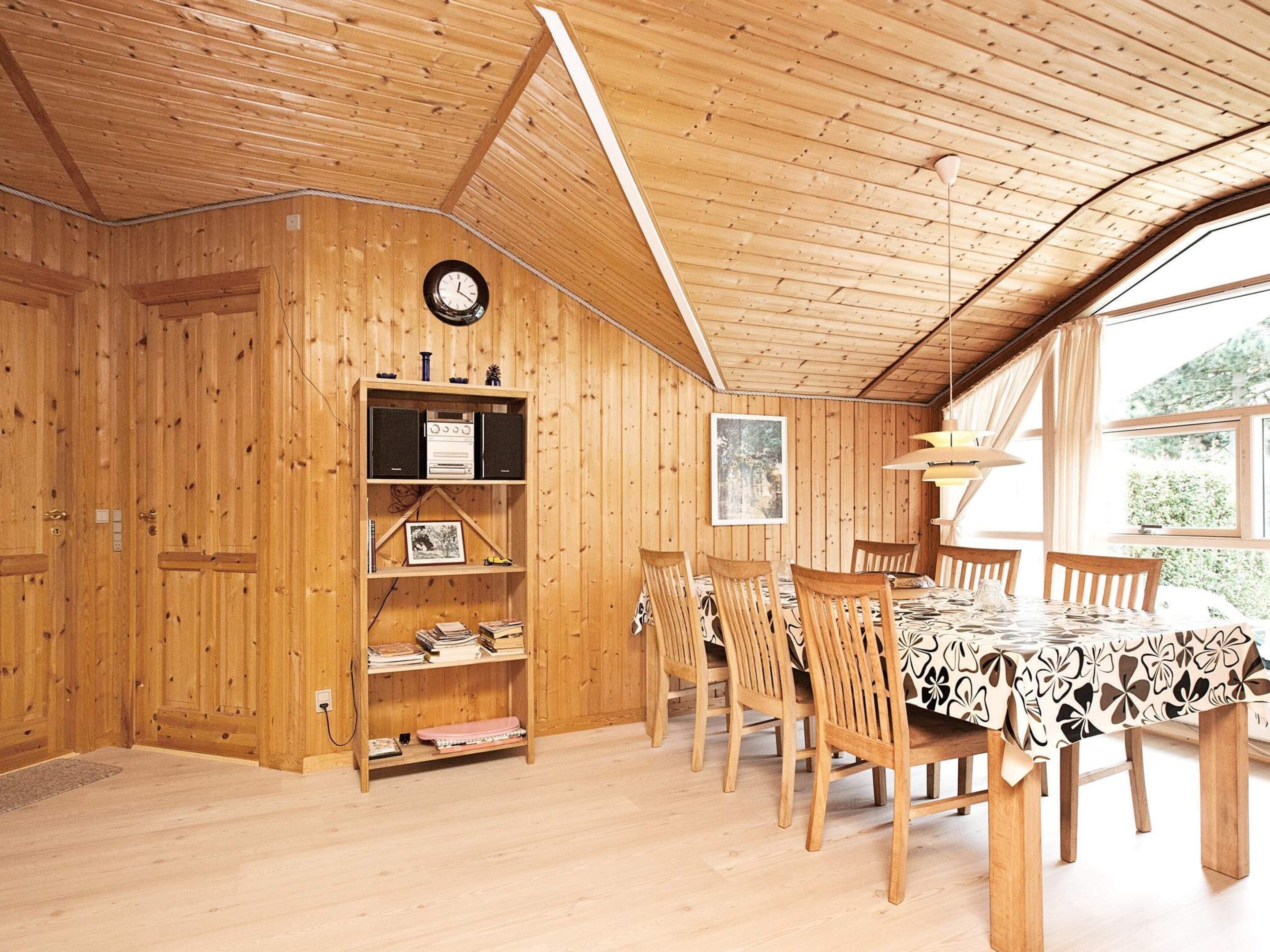 A wooden interior with a dining area, bookshelves, and a clock.