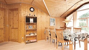 A wooden interior with a dining area, bookshelves, and a clock.