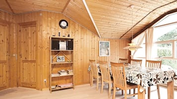 A wooden interior with a dining area, bookshelves, and a clock.