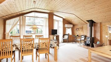 Ein geräumiger Raum mit hoher Decke, Holzwänden, einem Essbereich mit Stühlen und Tisch, einem Fernseher und einem Kamin.