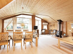 A spacious room with a high ceiling, wooden walls, a dining area with chairs and a table, a television, and a fireplace.