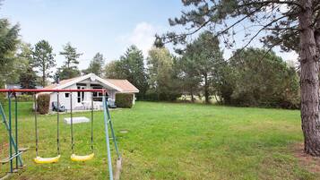 A residential property with a grassy yard, a swing set, and a house with a red roof.